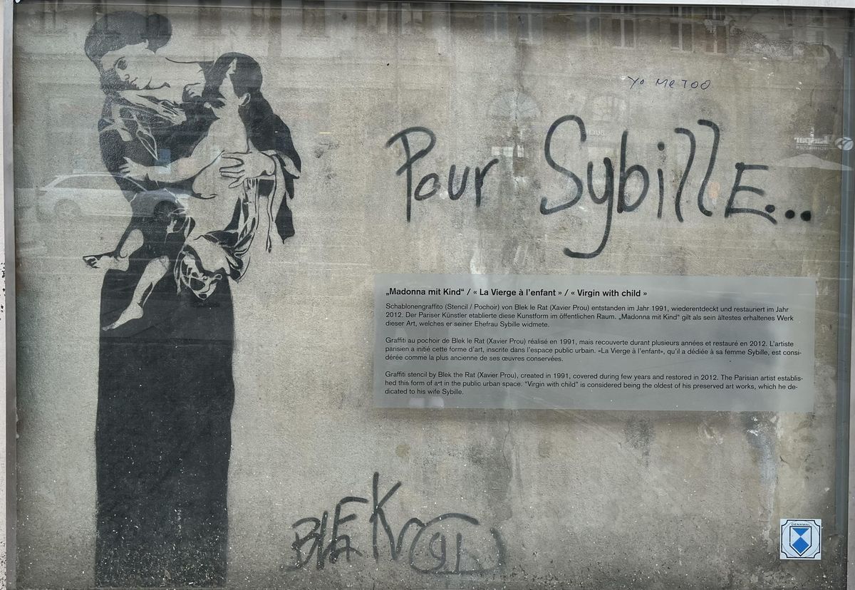 zur Vergrößerungsansicht des Bildes: Graffiti (Madonna mit Kind) hinter Glas und mit Erläuterung an einer Hauswand in der Südvorstadt