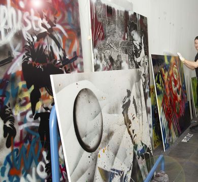 Blick in den Ausstellungsraum, an den Wänden stehen großformatige Platten in bunten Farben, ein Mitarbeiter der Kustodie sortiert die Kunstwerke