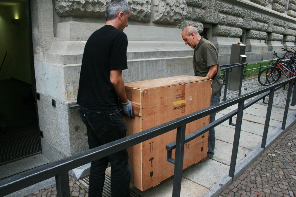 zur Vergrößerungsansicht des Bildes: Ein Gemälde in einer großen Kiste wird durch die Mitarbeiter zur Universitätsbibliothek getragen.