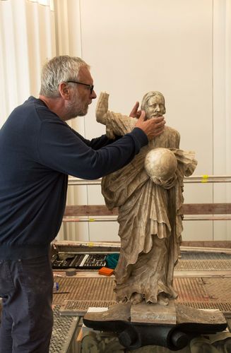 Der Steinrestaurator Thomas Schubert bei der Montage des Christus-Kopfes, unterstützt durch Kustodie-Mitarbeiter Nico Hempel. Im Vordergrund ist eine Rasterfotografie des originalen Kopfes aus den 1950er Jahren zu sehen.