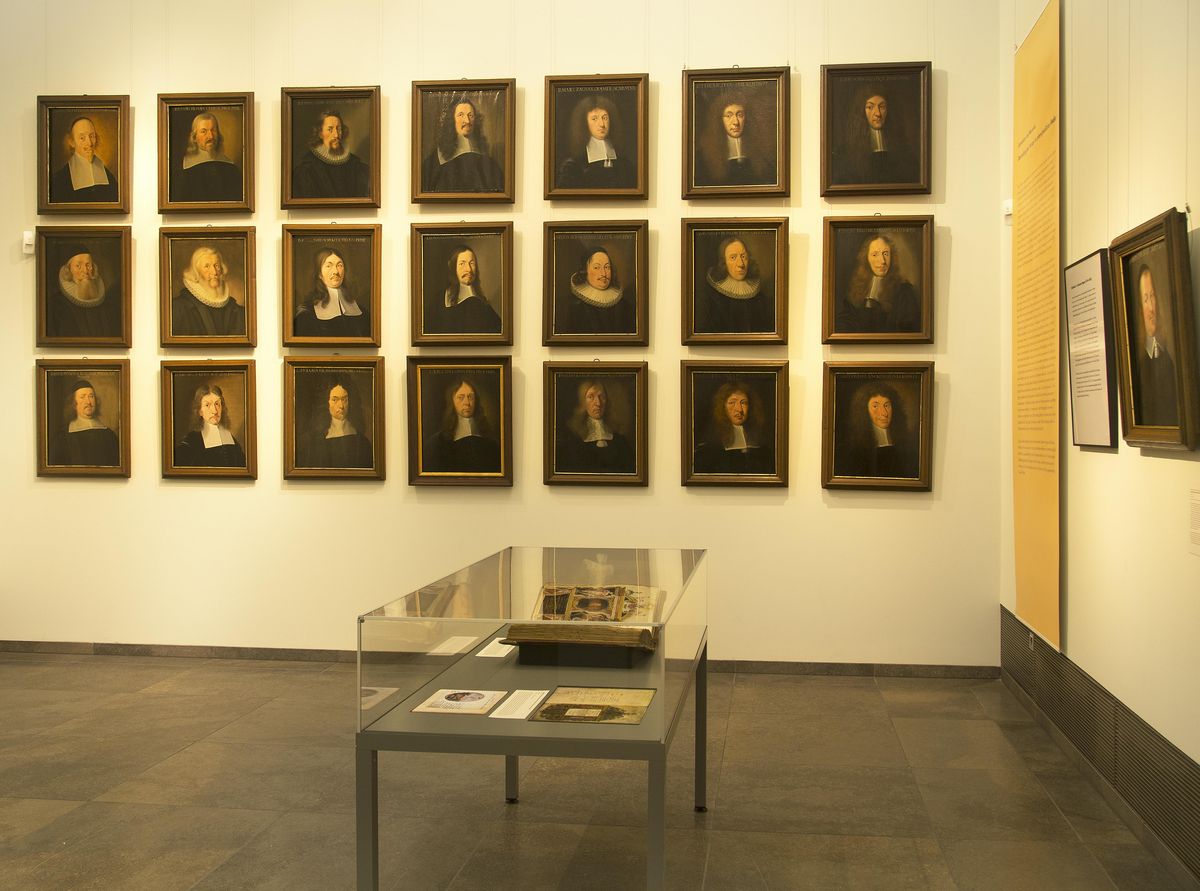 Blick in einen Galerieraum, an der Wand hängt eine Porträtgalerie in einer Blockhängung von 21 Gemälden, die Porträts zeigen Professoren der Universität des 17. Jahrhunderts