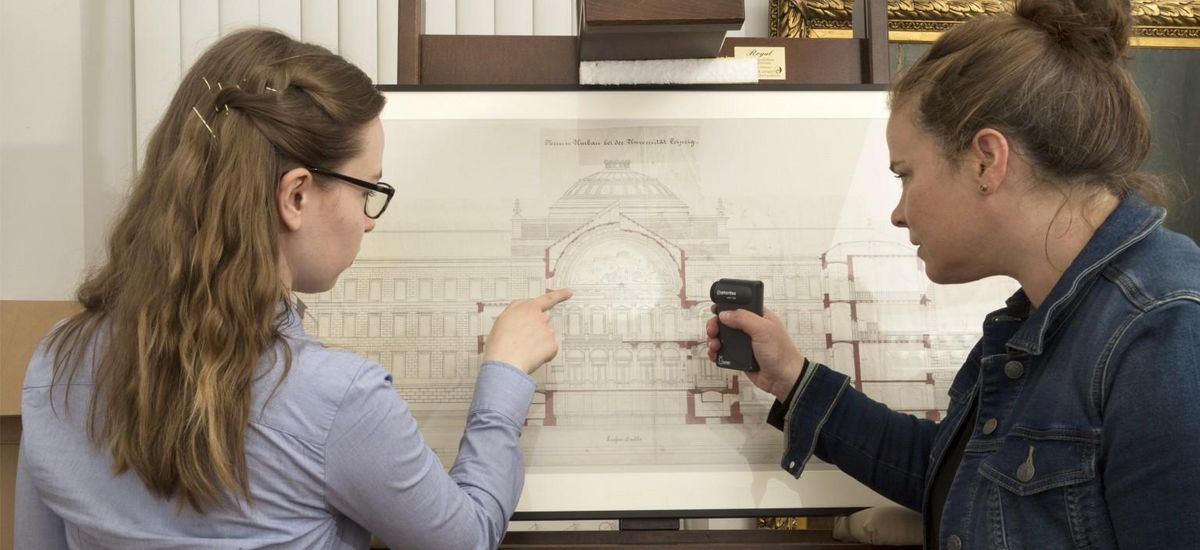 Dr. Christine Hübner betrachtet mit einer Studentin eine Architekturzeichnung auf einer Tafel.