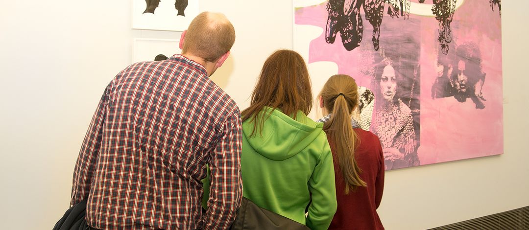 Eine Familie (Vater, Mutter, Tochter im Teenager-Alter) betrachtet ein Gemälde zeitgenössischer Kunst