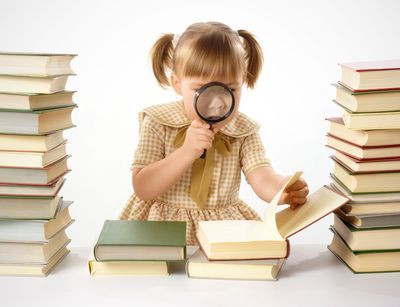 Ein junges Mädchen guckt mit einer Lupe in ein aufgeschlagenes Buch, um sie herum stapeln sich Bücherberge