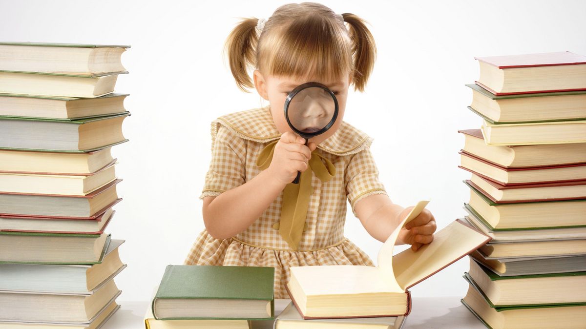 zur Vergrößerungsansicht des Bildes: Ein junges Mädchen guckt mit einer Lupe in ein aufgeschlagenes Buch, um sie herum stapeln sich Bücherberge
