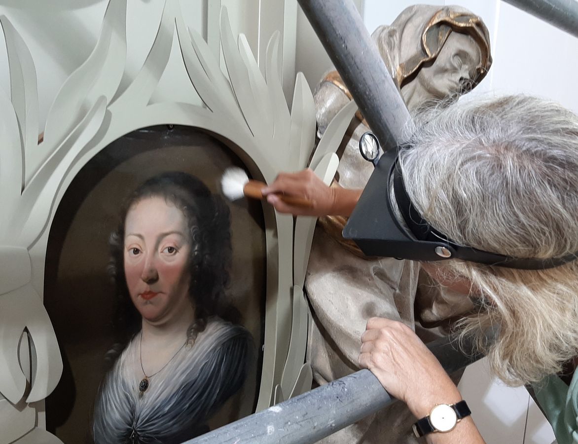 zur Vergrößerungsansicht des Bildes: Eine Restauratorin reinigt das Epitaph der Anna Regina Welsch mit einem Pinsel.
