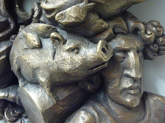 Detail einer Bronzeplastik des Künstlers, zu sehen ist rechts der Kopf einer männlichen Figur, links daneben sitzt ein Schweinchen, darüber sind Fische zu sehen